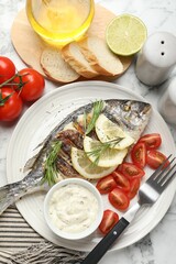 Tasty roasted dorado fish with bread, sauce, tomatoes and lemon on white marble table, flat lay. Homemade seafood dish