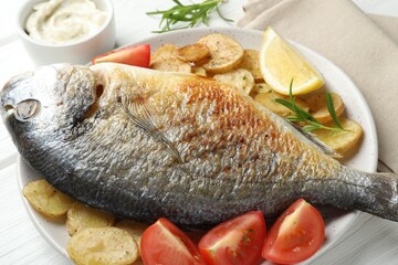 Tasty roasted dorado fish served with vegetables and sauce on white wooden table, closeup. Homemade seafood dish