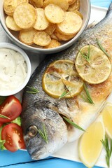 Tasty roasted dorado fish served with vegetables and sauce on light blue wooden table, flat lay. Homemade seafood dish