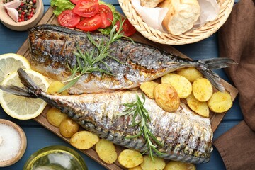 Tasty roasted mackerels served with spices and vegetables on blue wooden table, flat lay. Homemade seafood dish