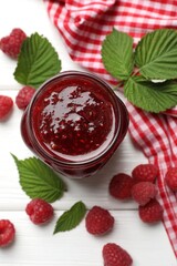 Tasty jam, fresh ripe raspberries and leaves on white wooden table, flat lay.