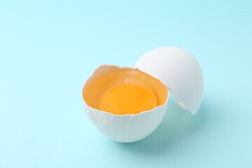 One broken chicken egg on light blue background, closeup