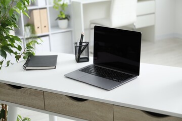 Stylish workplace with laptop, stationery and floral decor in office. Biophilic interior design