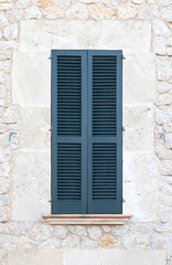 Fototapeta premium Closed blue wooden shutters on a traditional stone wall facade