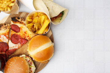 Different delicious fast food on white tiled table, flat lay. Space for text