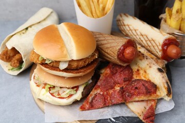 Different delicious fast food on grey table, closeup