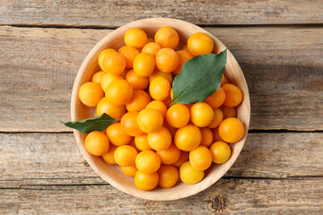 Ripe yellow cherry plums and leaves on wooden table, top view
