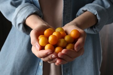 Woman holding heap of ripe yellow cherry plums indoors, closeup