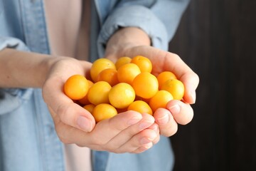 Woman holding heap of ripe yellow cherry plums indoors, closeup