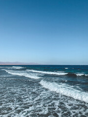 Fototapeta premium Bright blue ocean with strong waves rolling under a clear sky.