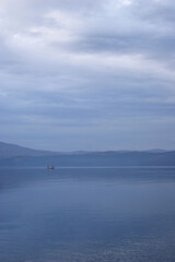 Serenity on the lake during twilight reveals a lone boat gliding through calm waters surrounded by gentle mountains