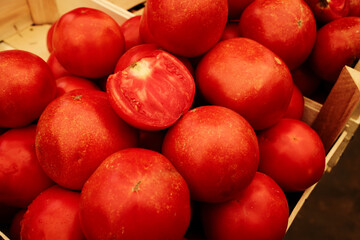 Fresh ripe tomatoes in a wooden crate, with one cut open showing juicy texture. Organic vegetables for cooking, salads, and healthy diets