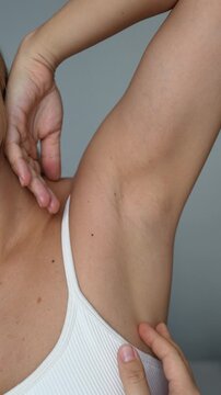 Vertical video of a young woman stroking the armpit showing her smooth skin after depilation on a grey background. The result of laser hair removal