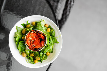 Healthy vegetarian meal with leafy green salad, olives, and baked vegetable terrine on a white plate, served on glass table with soft background textures.
