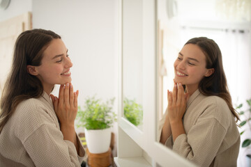 Woman smiling at herself in the mirror during morning skincare routine.