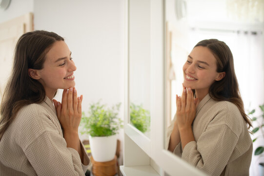 Woman smiling at herself in the mirror during morning skincare routine.
