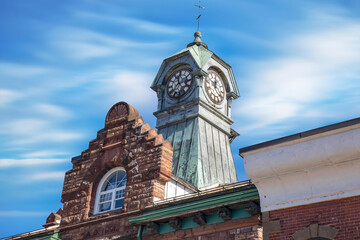 Daytime view of clocktower with copper siding, foreground limestone facade with round window, blue skies, nobody