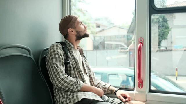 Young man with backpack sitting on a bus, looking out the window thoughtfully. Urban transport and daily commute concept. Horizontal 4k slow motion footage