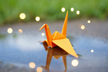An origami crane rests on a reflective surface, surrounded by bokeh lights