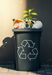 Black recycling bin filled with plastic waste sprouts a green plant, symbolizing hope, sustainability, and environmental responsibility amid pollution.