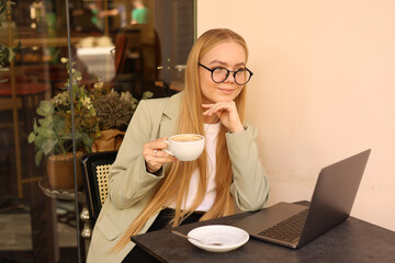 Woman drinking coffee and working on laptop in cafe.