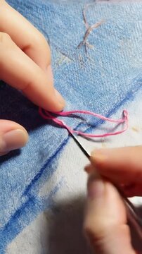 Close-up of hands using a seam ripper to carefully remove pink embroidery stitches