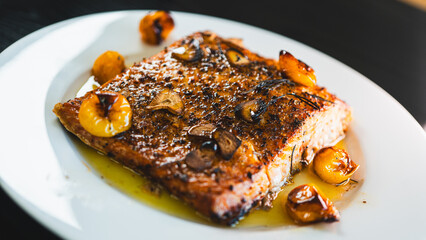 Succulent pan-seared salmon drizzled with olive oil, topped with crispy burnt garlic slices and roasted yellow tomatoes. Gourmet plating, highlighting textures and colors for food branding and culinar