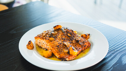 Succulent pan-seared salmon drizzled with olive oil, topped with crispy burnt garlic slices and roasted yellow tomatoes. Gourmet plating, highlighting textures and colors for food branding and culinar