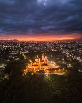 oma a&eacute;rea de dron de la Catedral de Puebla al atardecer, con la ciudad iluminada y cielo c&aacute;lido, perfecta para turismo, arquitectura y patrimonio cultural mexicano