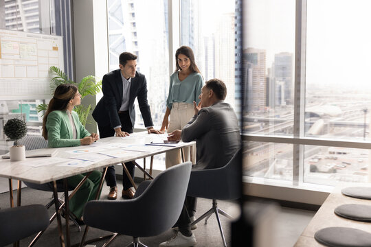 Group of four professionals engaged in srategic business planning meeting in high-rise office with panoramic city view. Team brainstorming ideas, making important decisions. Seminar, briefing event