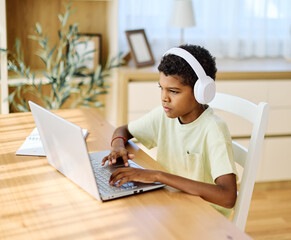 Portrait of a teenage boy  having fun using laptop wearing headphones and listening to the sound or music or doing homework and learning with laptop at home
