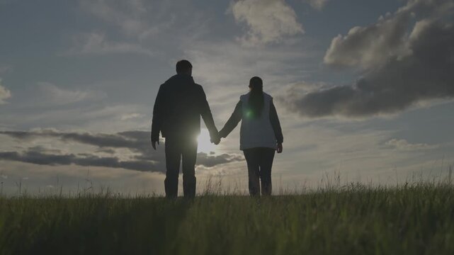 man and woman stand at sunset holding hands, romantic evening of two people, farming, teamwork in the sun, trust and equality of businessmen, agronomists concept, farmers working on the land.
