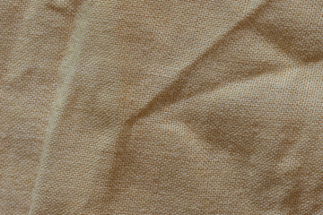 Detailed macro of beige cloth texture showing its weave and organic folds. Perfect for use in eco-friendly design, craft visuals, textile samples, or minimalistic backgrounds