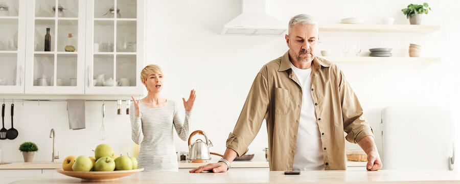 Couple have disagreement at kitchen at home, quarrel in family and problems in relationships. Annoyed middle aged woman yelling at offended husband on modern kitchen interior, panorama, copy space - Powered by Adobe
