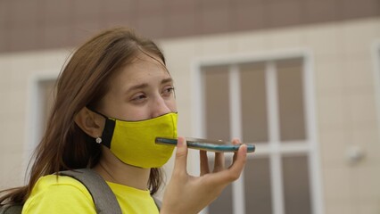 Schoolgirl girl in a mask with a backpack talks on a smartphone online, modern trends in technological progress, protect herself from coronavirus infection, air filtration.