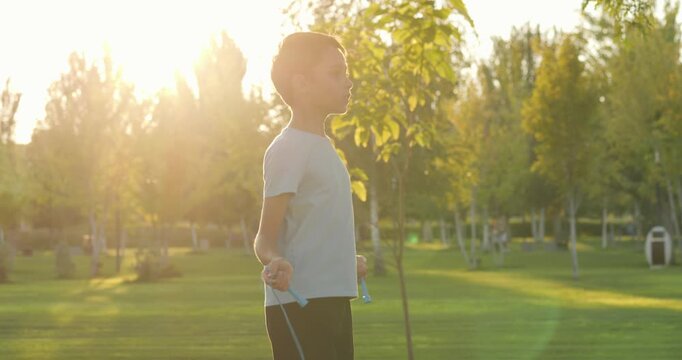 Energetic happy kid jumps rope in sunny park during golden hour. Kid enjoys outdoor exercise movement freedom in nature sunset. Joyful kid active play wellness. Summer fitness healthy lifestyle child.