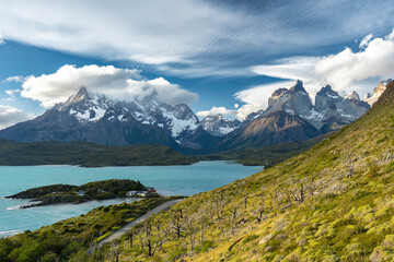 Majestic golden hour light illuminates the iconic Cuernos del Paine mountain range, overlooking the serene Lago Pehoé with its scenic footbridge in Torres del Paine National Park, Patagonia.