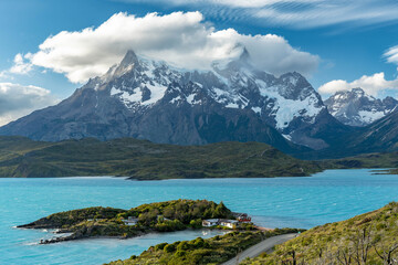 Majestic golden hour light illuminates the iconic Cuernos del Paine mountain range, overlooking the serene Lago Pehoé with its scenic footbridge in Torres del Paine National Park, Patagonia.
