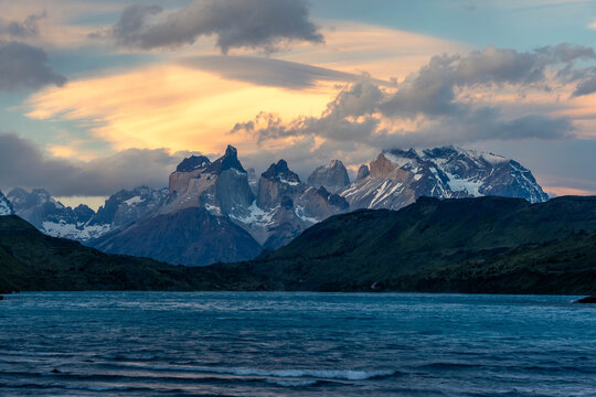 Golden hour light illuminates the iconic Cuernos del Paine peaks under a dramatic, fiery sky with lenticular clouds in Torres del Paine National Park, Patagonia.