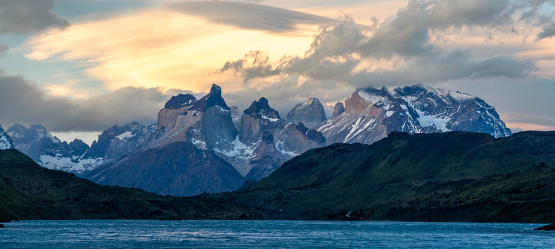 Golden hour light illuminates the iconic Cuernos del Paine peaks under a dramatic, fiery sky with lenticular clouds in Torres del Paine National Park, Patagonia.