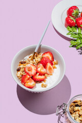 Granola or muesli with natural greek yogurt, strawberry in a bowl on a bright violet background with berries.