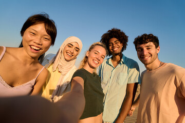 Obraz premium Happy multi ethnic friends taking selfie at sunset, enjoying summer vacation