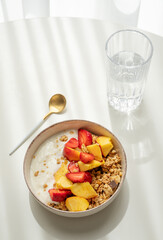 Granola or muesli with natural greek yogurt, strawberry and peach in a bowl on a white table near window