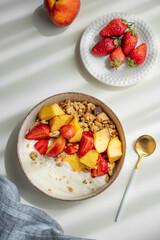 Granola or muesli with natural greek yogurt, strawberry and peach in a bowl on a white background