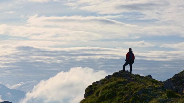 Silhouette of a hiker enjoying a fantastic view from the top of a cliff of clouds and mist moving below him. Hiking, mountaineering, outdoor activity, sports. 
