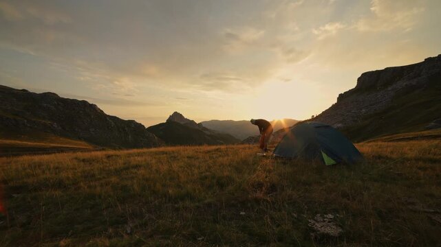 Sunrise on the mountains. A man sets up a tent and enjoys the first rays of the rising sun. Hiking, outdoor, activity, nature. Active lifestyle, sports. 