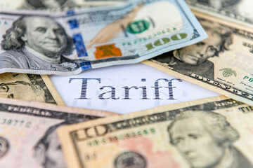 A tariff tax concept with various US Dollar bills surrounding the printed word tariff.