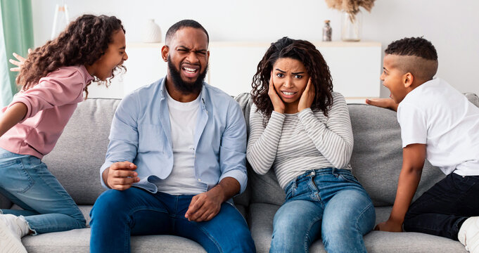 Problems Of Parenthood Concept. Portrait of angry African American kids having quarrel over their shocked parents. Boy and girl screaming at each other. Scared mother and father covering ears