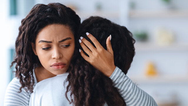 Worried young black mother comforting her crying daughter, hugging her and whispering words of support, closeup. African american woman embracing female kid, touching her head and saying something - Powered by Adobe
