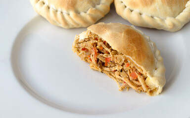 Plato con empanadas de pollo exquisitas y jugosas, con abundante relleno y cortada o partida por la mitad.